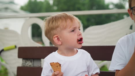 a little boy is holding an ice cream cone, with chocolate smeared all over his mouth, while he sticks his tongue out, covered in chocolate