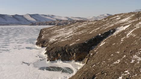 flight along the hilly coast with an opening view of a frozen lake and rocks in the distance with houses