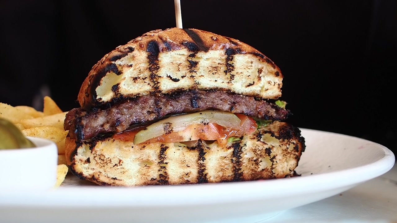 Person's Hands Lifting a Gourmet Grilled Burger from a Plate