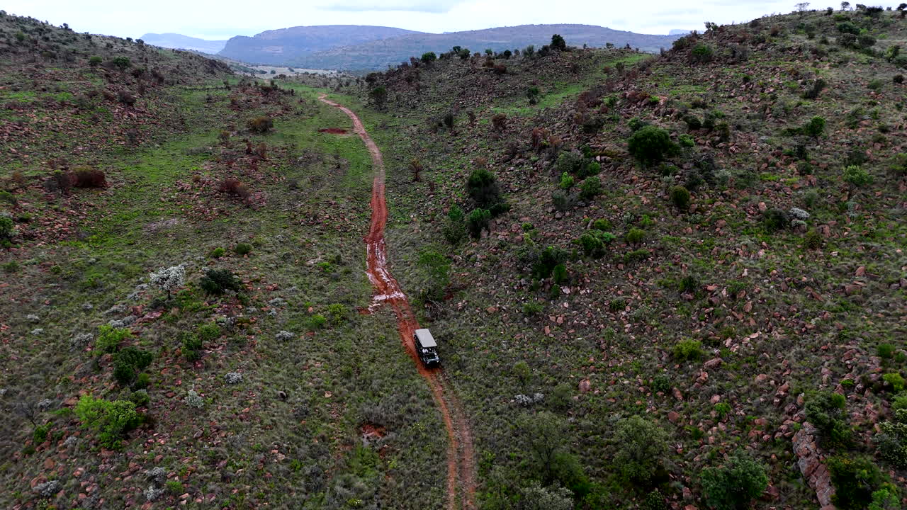 A green safari vehicle navigates a muddy mountain trail in a vast, rugged landscape