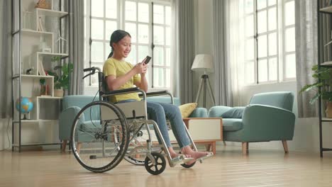 asian kid girl sitting in a wheelchair while smiling and using smart phone at home