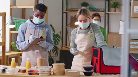 colegas multiétnicos con máscaras preparando pedidos de comida para la entrega