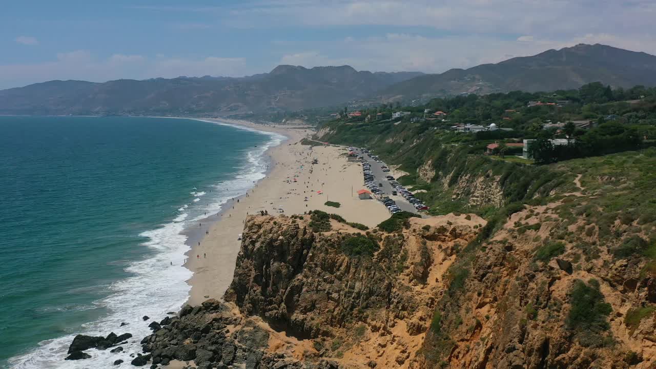 태평양의 파도가 해변에 충돌하는 동안 관광객들이 캘리포니아 미국의 더운 여름날 아래 해변을 즐기는 동안 말리부 절벽 해안선의 높은 고도 공중 전망