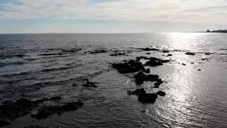 Luftaufnahme-Von-Steinen-Mit-Enten-Im-Meer-An-Einem-Sonnigen-Tag-Und-Der-Skyline-Im-Hintergrund-Am-Pier-Von-Montevideo,-Montevideo,-Uruguay