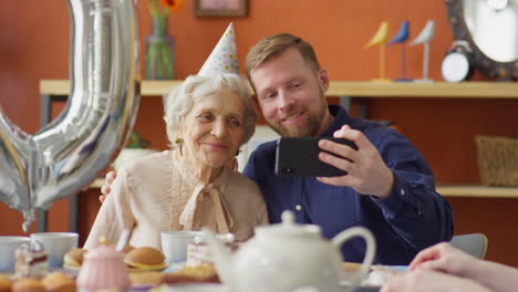 cheerful man taking selfie with grandma on birthday dinner