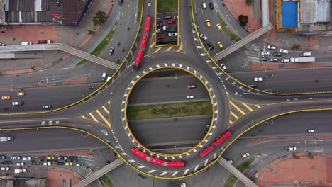 una toma a vista de pájaro con un dron de 4k que desciende en una intersección de puntos redondos con autobuses articulados rojos, taxis y otros vehículos que giran desde la calle tercera hasta la avenida 30 en bogotá, colombia