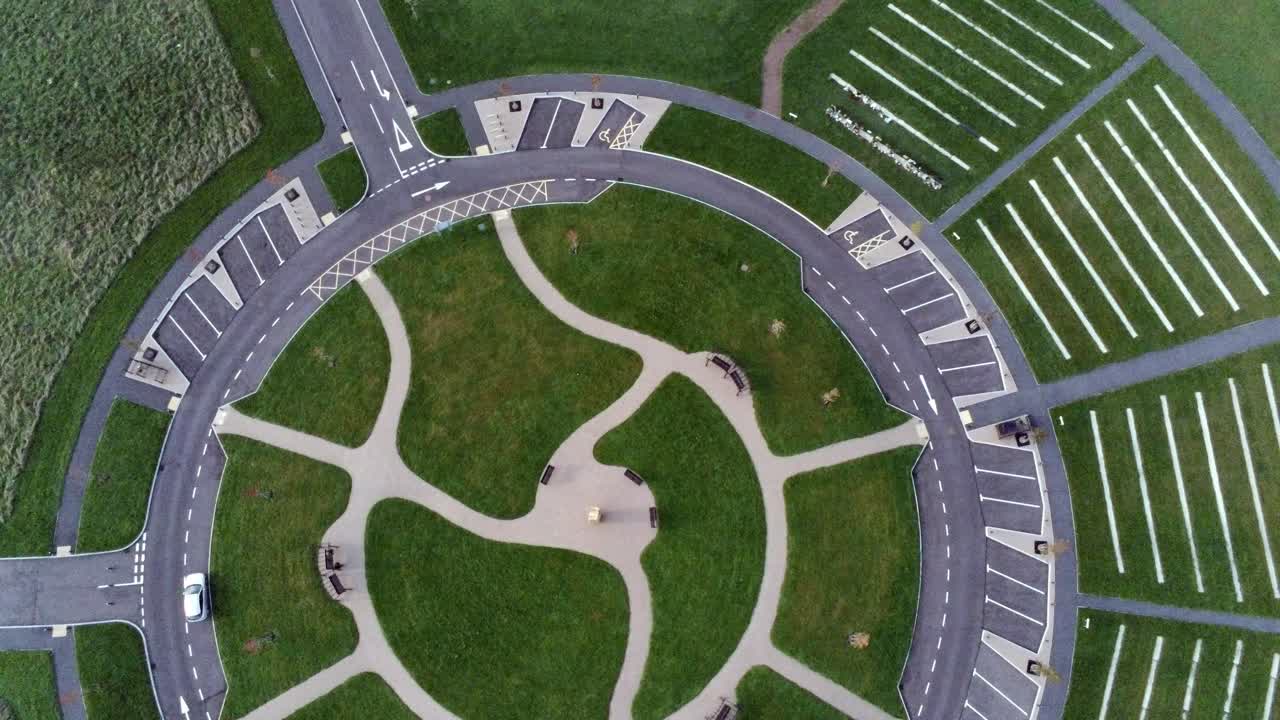 Circular design aerial rising rotate view above ornamental landscaped cemetery garden with parking around outside