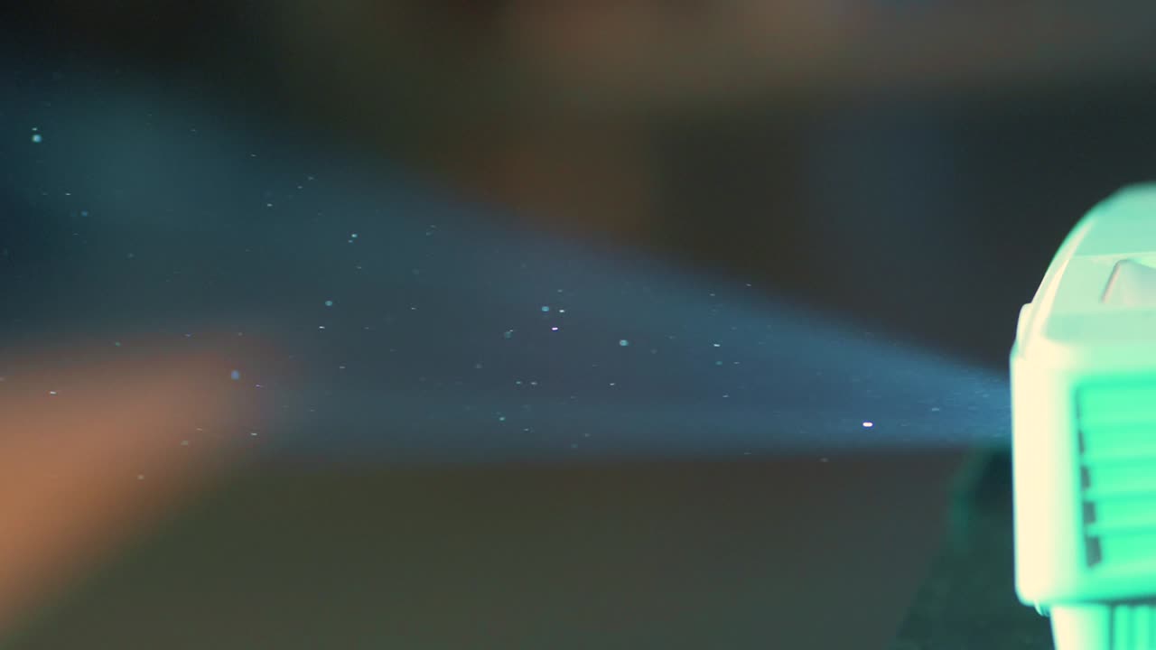 먼지 입자들은 공중에서 떠다니는 작은 별처럼 보이며, 옛날 프로젝터의 빛에 비추어 어두운 방에서 빛을 비추고 있습니다.