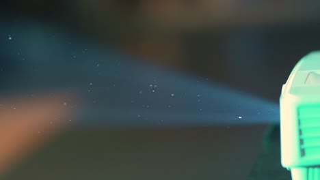 las partículas de polvo parecen pequeñas estrellas mientras flotan en el aire iluminadas por la luz de un proyector vintage que brilla en una habitación oscura.