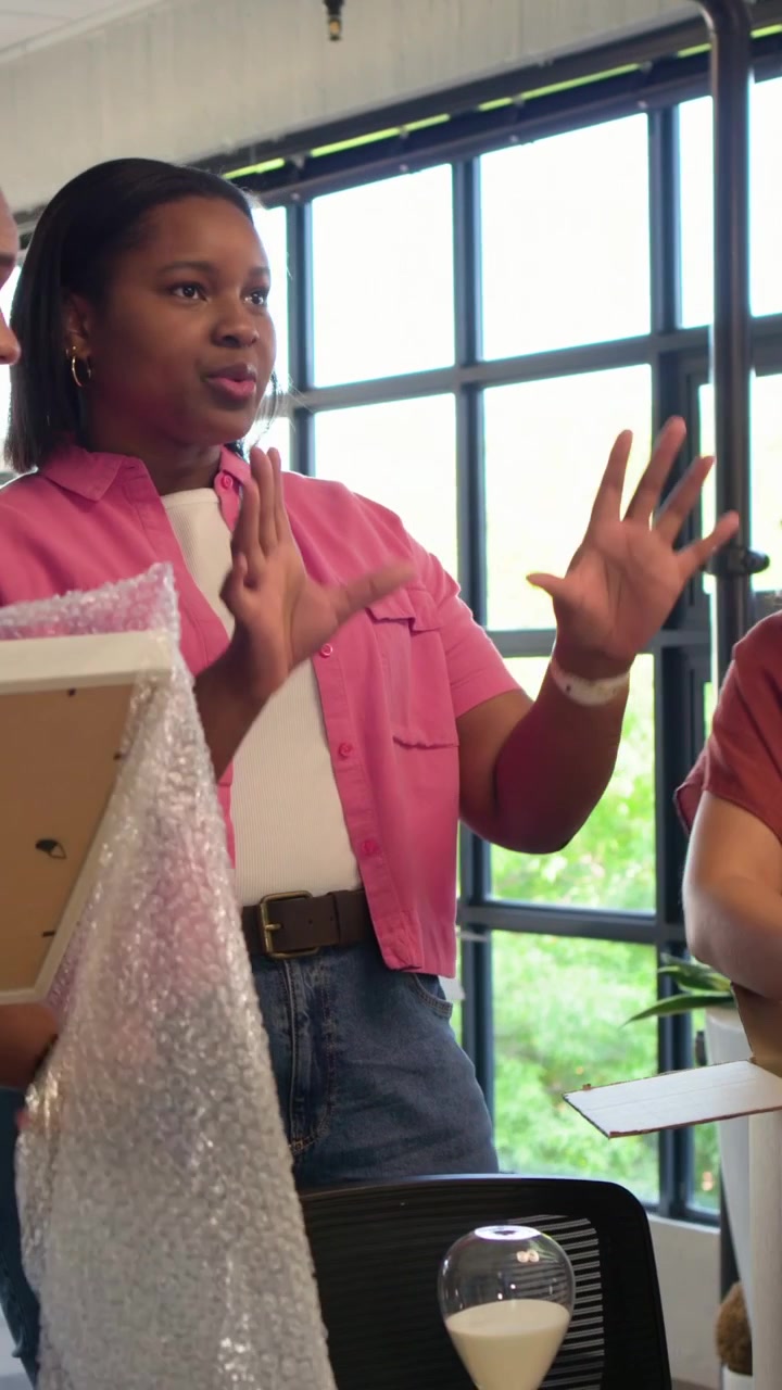 Vertical video: Man closing in, unpacking frame by window, woman in pink shirt checking hourglass