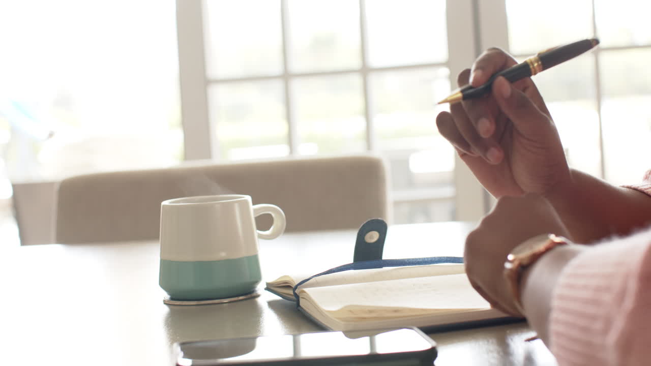 una mujer afroamericana escribe en un cuaderno, en la cocina de su casa.
