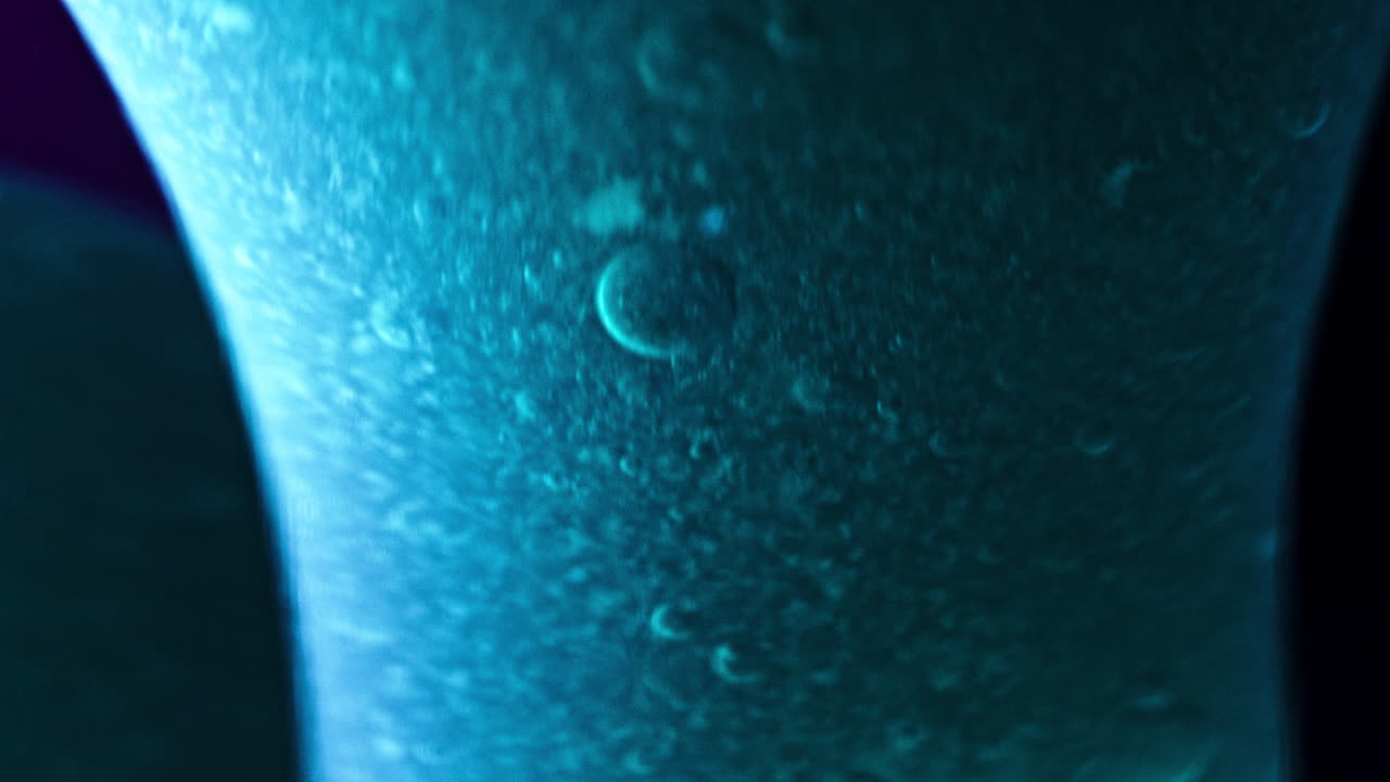 Abstract liquid mixture with bubbles in a vibrant blue light, macro shot, extreme close-up focus