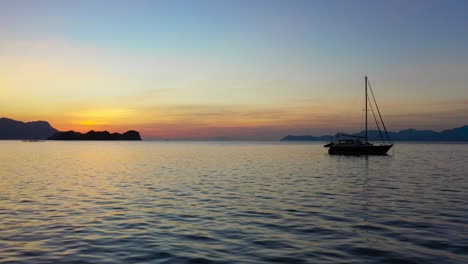 beautiful orange sunset above the sea surface with a sail boat, sun reflection , cinematic aerial view of langkawi island, malaysia