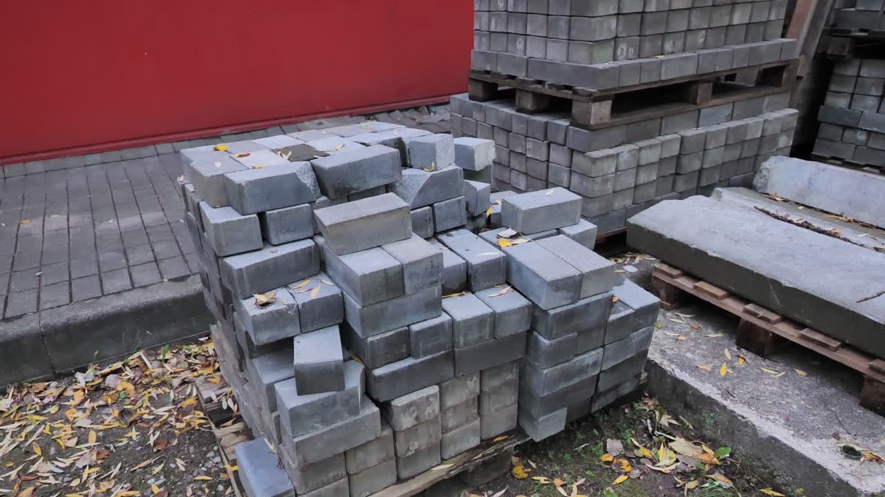 Gray bricks stacked neatly on pallet beside pavement with scattered autumn leaves