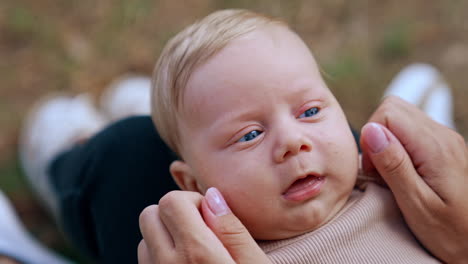 blond baby boy with adorable blue eyes lies on mom's laps. mother touches her kid's cheeks and nose. close up.