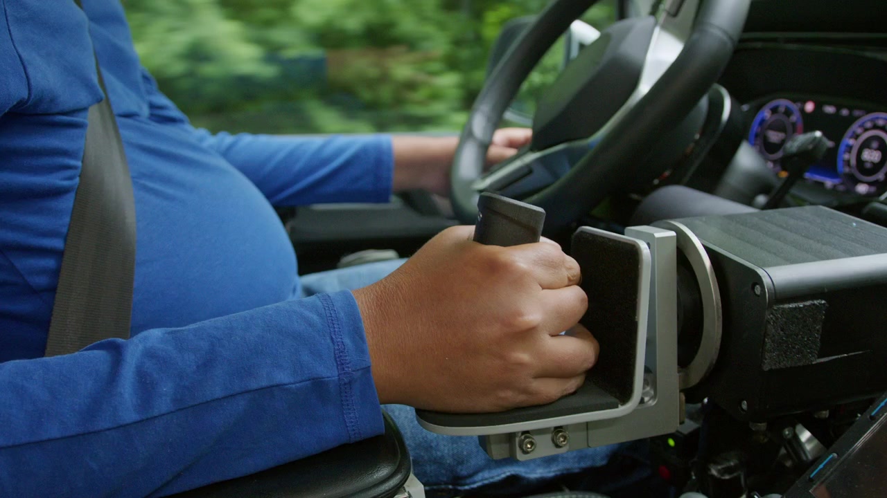 Driver with a physical impairment using assistive technology on a car dashboard and adaptive hand