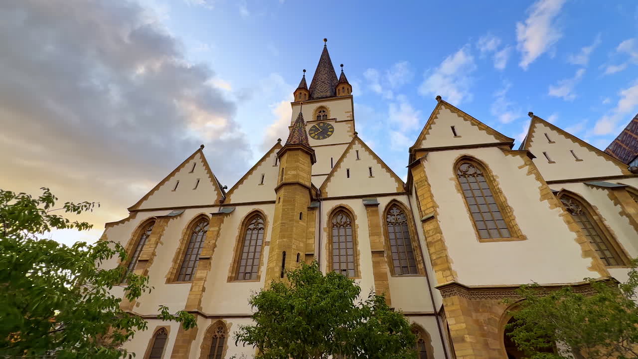 Front façade of Lutheran Cathedral of Saint Mary in Sibiu, Romania. Low angle view. Clouds lit by the setting sun in the blue sky at backdrop