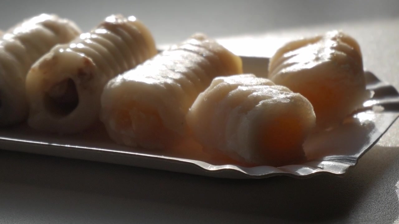 Tradizionali dolcetti di marzapane "huesos de santo" su un vassoio, retroilluminati dalla luce soffusa del giorno.