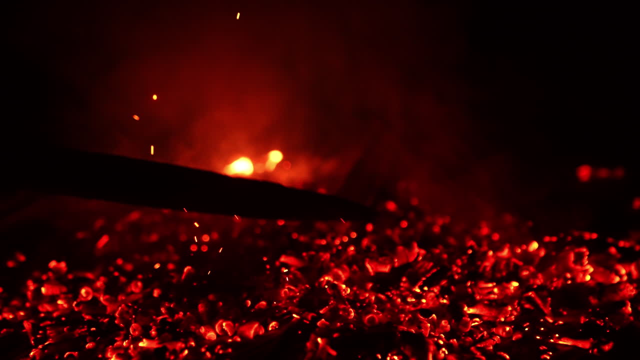 Unknown person moving the fire burning out. Smoldering embers sparkling beautifully. Black backdrop.