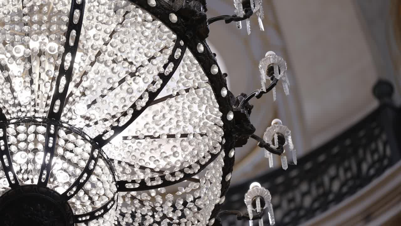 Elegant crystal chandelier viewed from below with decorative iron arms and ornate church ceiling