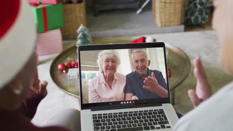 Diverse-senior-female-friends-using-laptop-for-christmas-video-call-with-happy-couple-on-screen