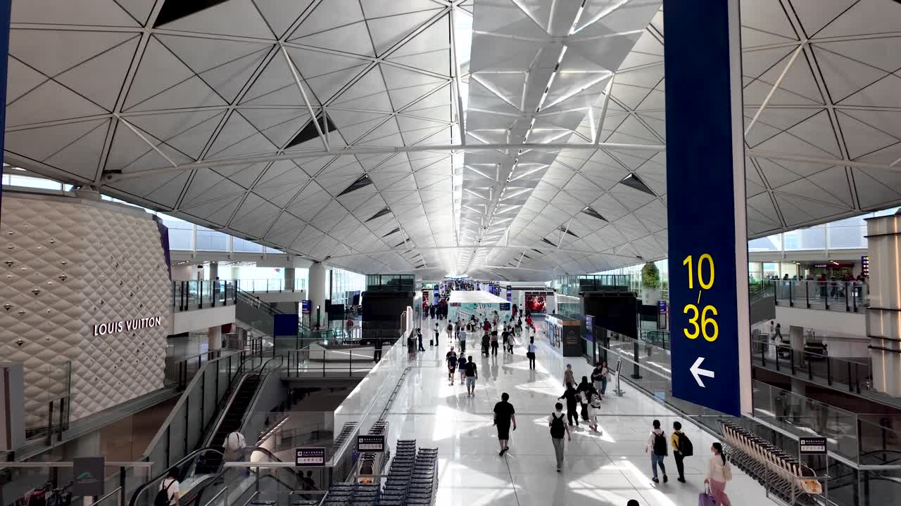 Elevated view of the spacious Hong Kong airport departure concourse featuring travelers and prominent gate numbers, capturing the modern architectural design and bustling atmosphere.