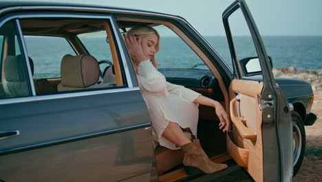 elegant woman posing auto with open door. girl sitting in retro car at sea shore