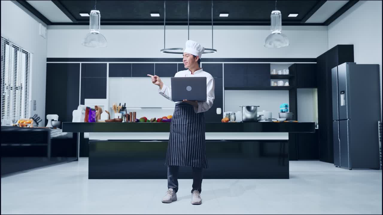 집 주방에 서 있는 동안 노트북을 사용하고 을 가리키는 아시아 남자 요리사의 몸이 가득 차 있습니다.