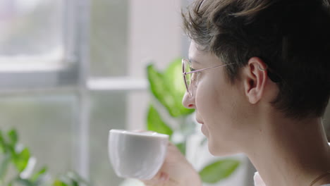 스마트폰을 사용하는 아름다운 백인 여성 집에서 커피를 마시고 편안한 아침을 즐기고 소셜 미디어 메시지를 검색하고 창밖을 바라보며 휴대전화로 문자 메시지를 보내고 안경을 쓰고 있습니다.