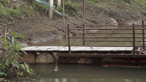 An-old-rusty-weathered-floating-pier-on-the-bank-of-the-Khwae-river,-a-metal-platform-made-with-old-oil-drums-giving-locals-access-to-the-houseboats-from-the-riverbank,-Kanchanaburi,-Thailand