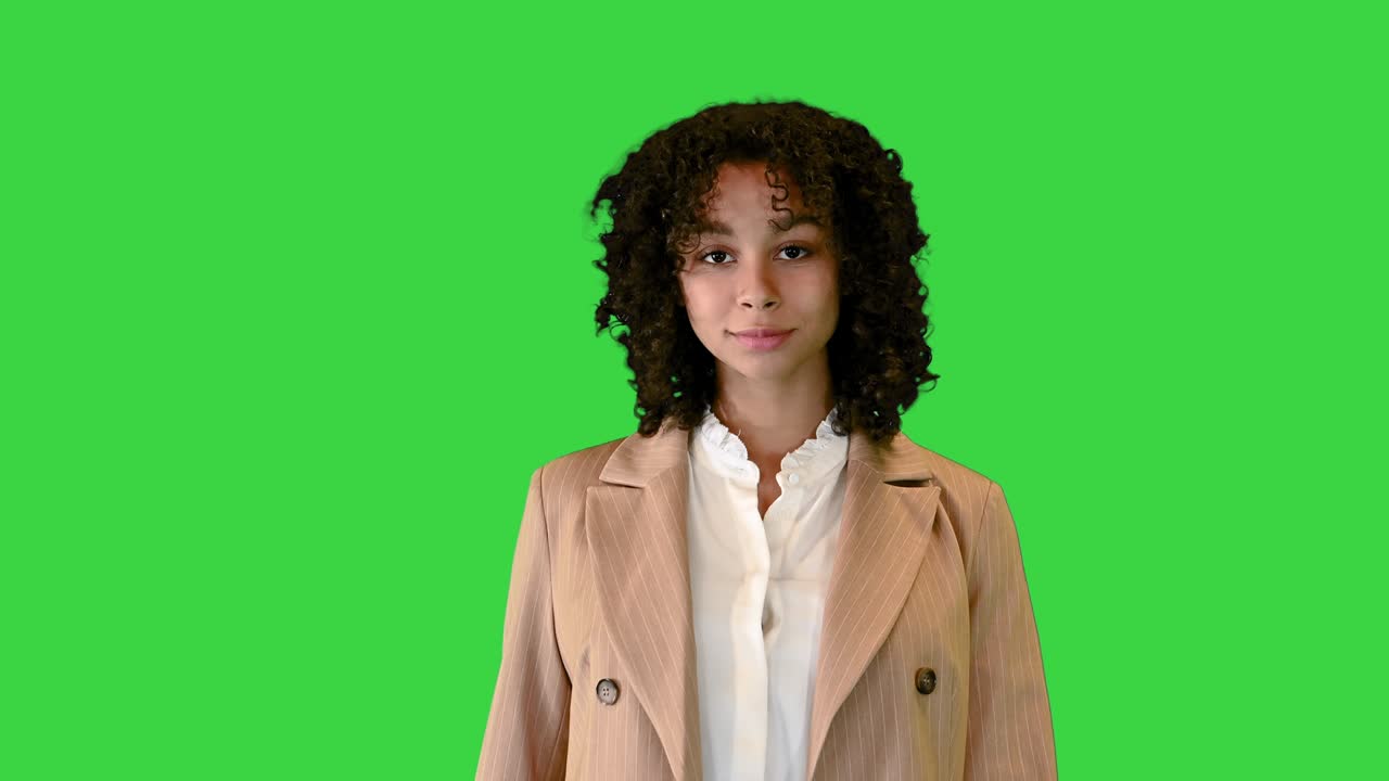 Glad ung dame med afrohår går på en grøn skærm, chroma key.