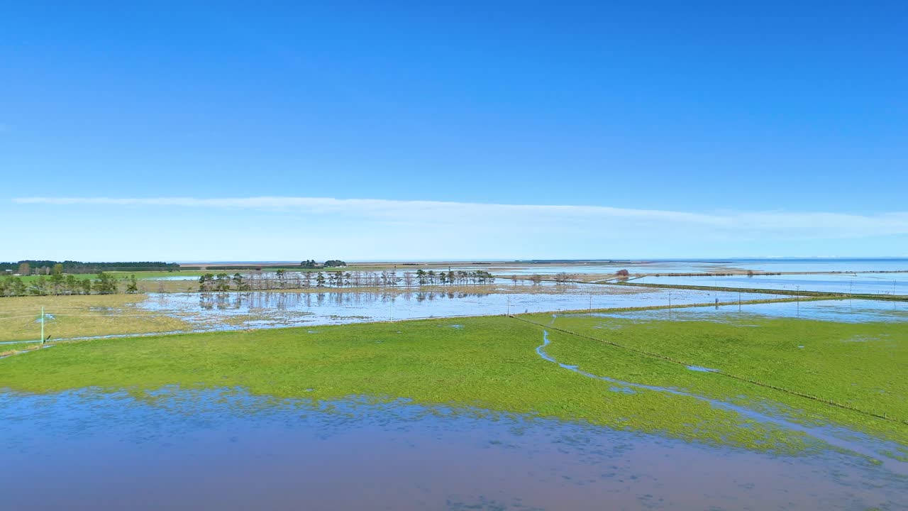 Aerial view of vibrant green fields and reflective water under clear blue skies in Akaroa, New Zealand