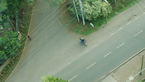 Vista-Aérea-Desde-Arriba-De-Una-Motocicleta-Que-Ingresa-A-Un-Camino-Rural-En-Kenia,-África