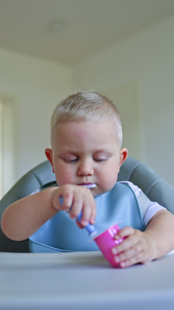 Two-year-old boy sits and eats yogurt independently. Toddler boy learns to eat independently. Dairy products are waiting for children