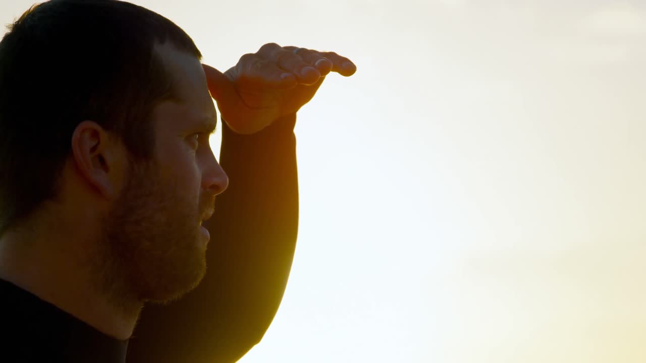 4k 해변에서 바다를 바라보는 보호 눈을 가진 중간 성인 백인 남성 서퍼의 측면 뷰