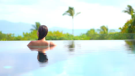 a woman in a swimming pool with her back to the camera looks out over the tropical ocean view