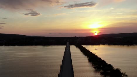 Aerial-above-long-bridge-over-river-at-sunrise,-sunset