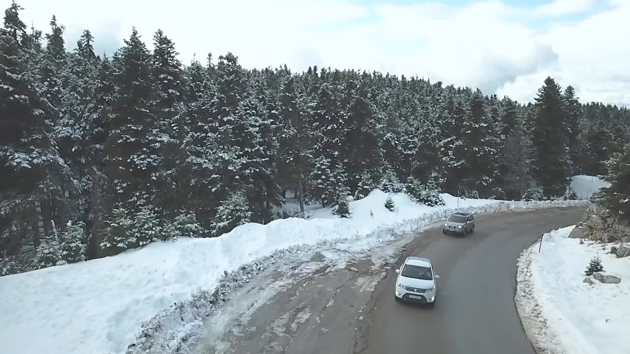 drones volando sobre los autos que se aproximan en una carretera de montaña rodeada de nieve en una tarde de invierno