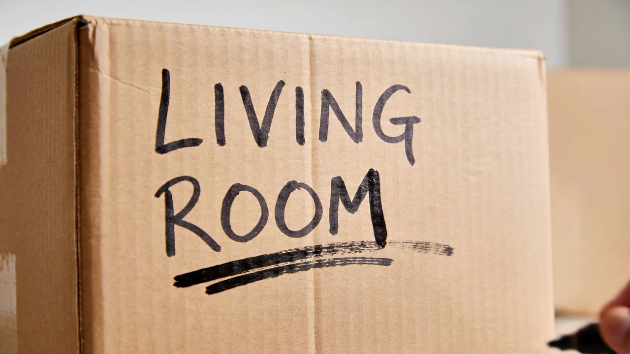 Marker touching box, right hand underlining LIVING ROOM label with black marker at home packing