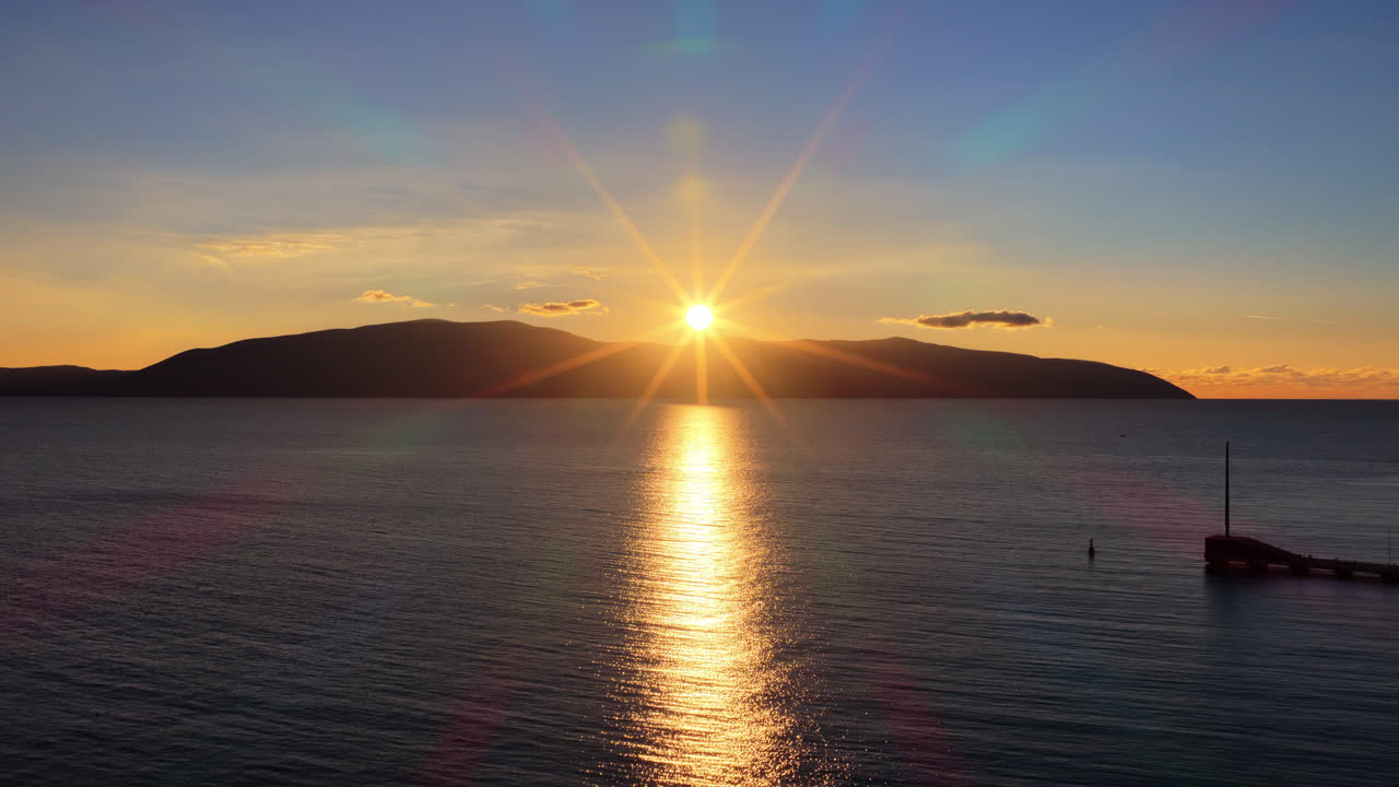 Aerial drone view of a sunset across the calm Adriatic Sea as the sun dips behind the mountains. Vlora, Albania