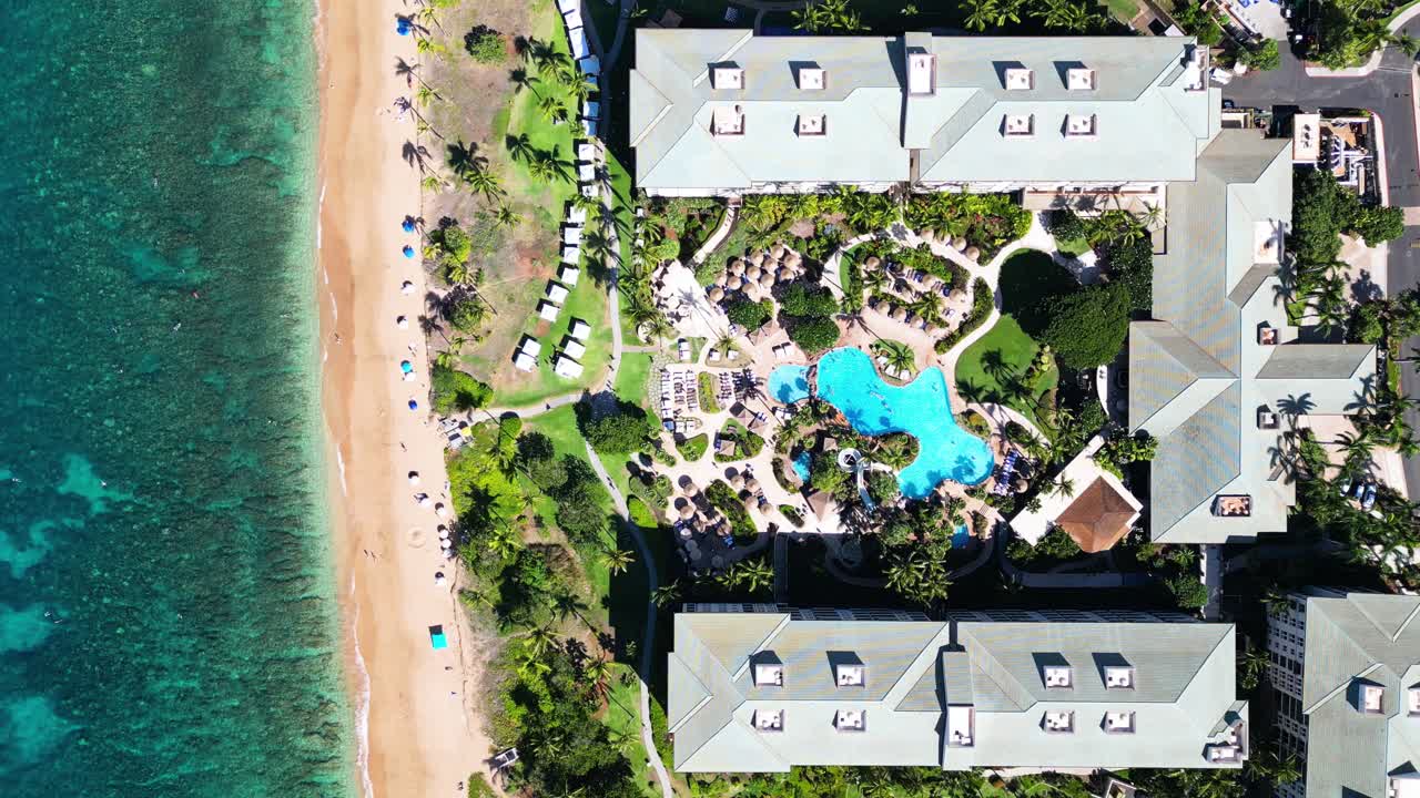 Top-down drone view: symmetric resort block open to beach with pool and crowds