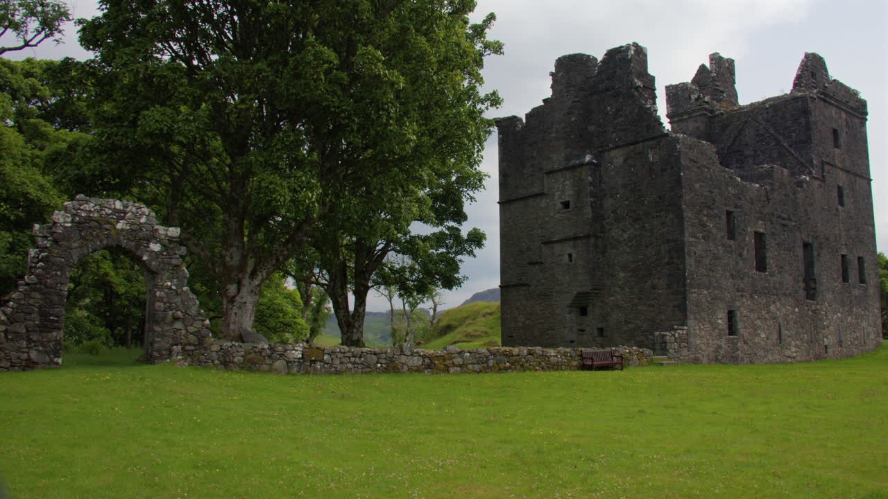 Wide shot looking across the grounds of Carnasserie Castle with stone arched gate,