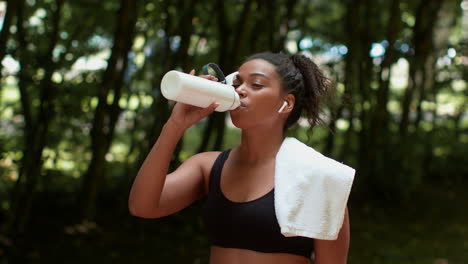 woman drinking water after workout in park