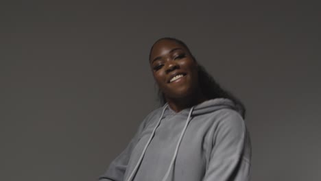 studio portrait shot of young woman wearing hoodie dancing with low key lighting against grey background 4