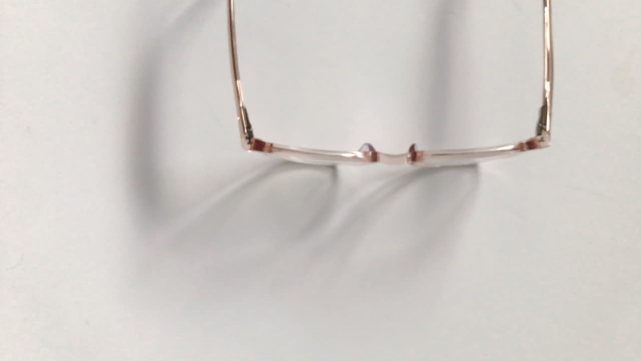 Modern eyeglasses in light colour lie on a white table, bright glasses frame, slow motion footage