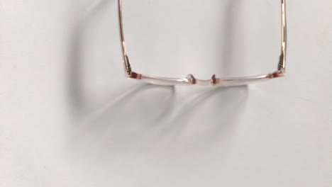 Modern-eyeglasses-in-light-colour-lie-on-a-white-table,-bright-glasses-frame,-slow-motion-footage