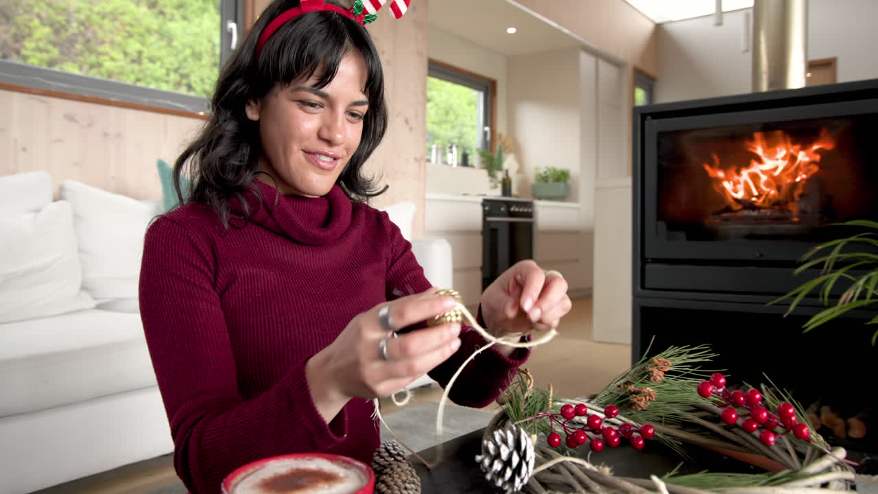Decorating Christmas wreath by fireplace, woman wearing festive headband, feeling joyful