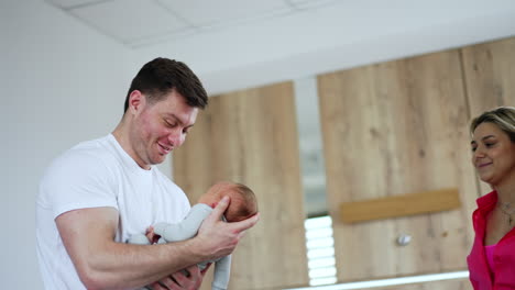 happy caucasian man holding his newborn child. smiling blonde mom comes up and looks at baby with love.
