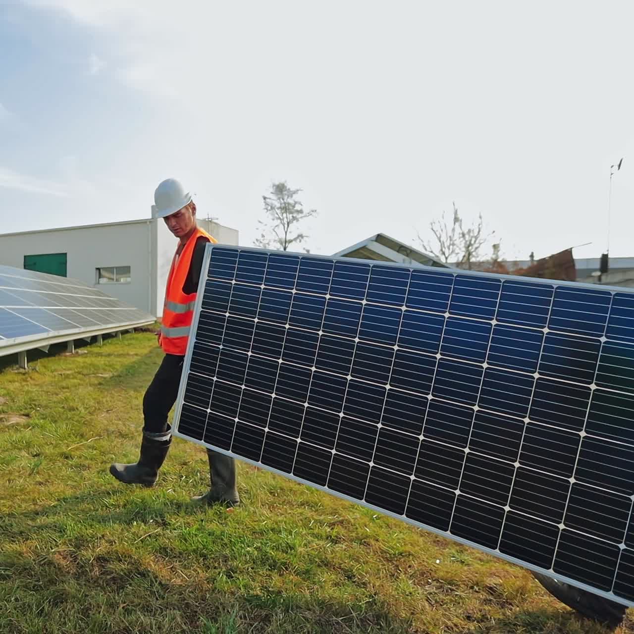 Workers carry solar panel to install on the grass. Technicians working with sunny battery on the farm. Alternative green energy.