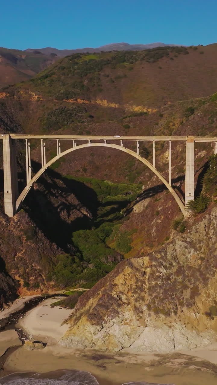 Arched bridge over the gap between the mountains. Sunlit mountains of California in the bright rays of sun. Aerial perspective. Vertical video